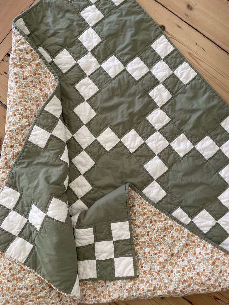 a green and white quilt on top of a wooden floor