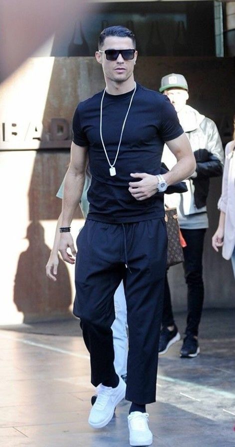 a man in black shirt and white pants walking down the street with his hand on his hip