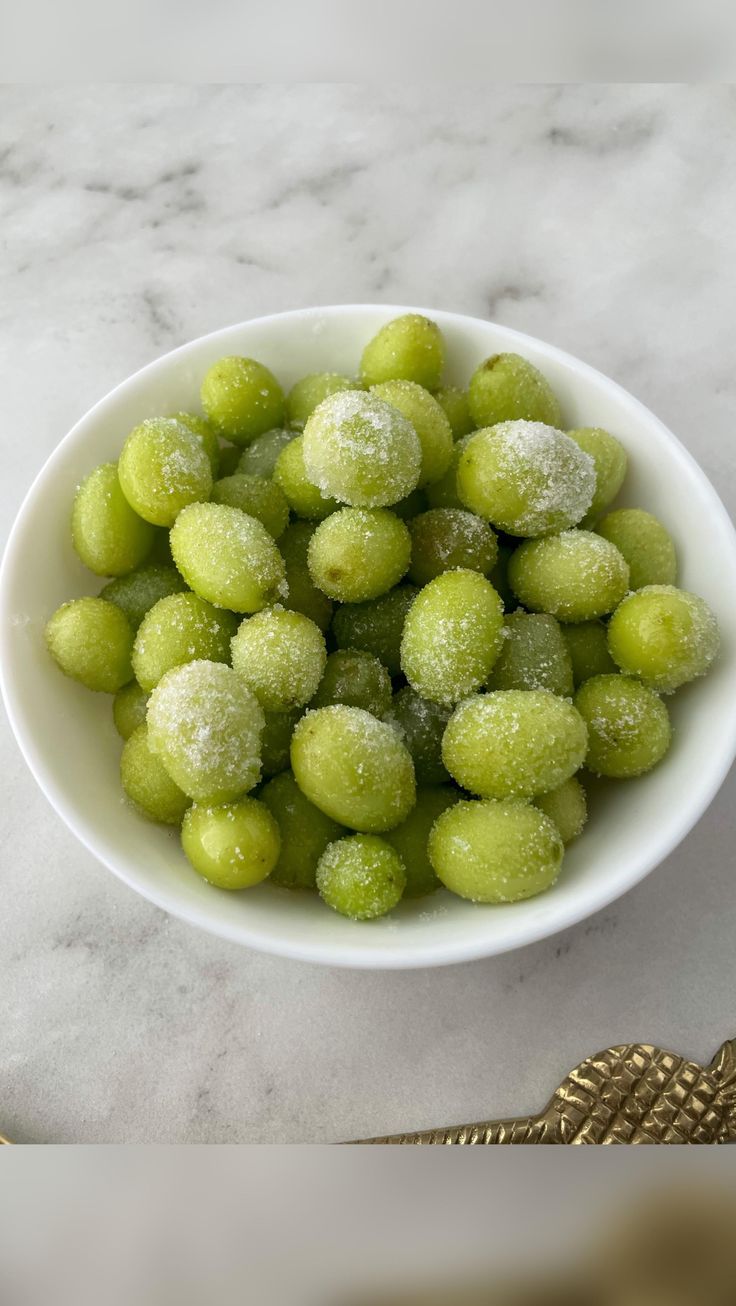 a white bowl filled with green grapes covered in powdered sugar on top of a marble counter