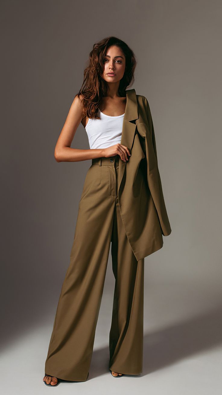 a woman standing in front of a gray background wearing a tan suit and white tank top