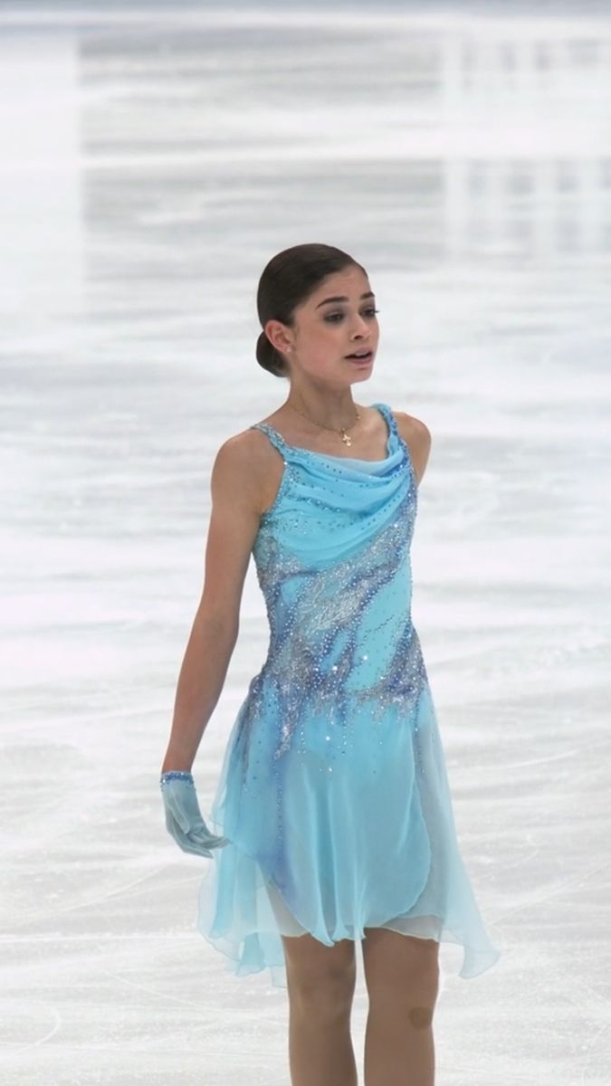 a woman in a blue dress skating on an ice - covered surface with her hands behind her back