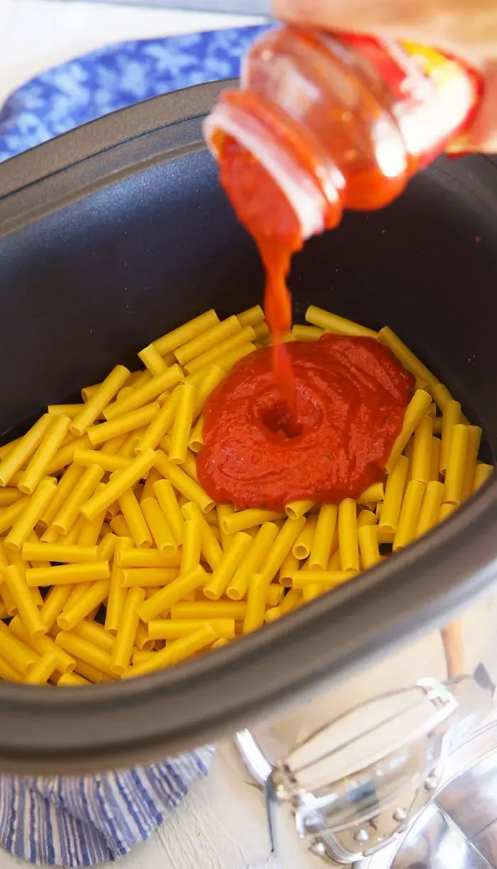 the sauce is being poured on top of macaroni and cheese