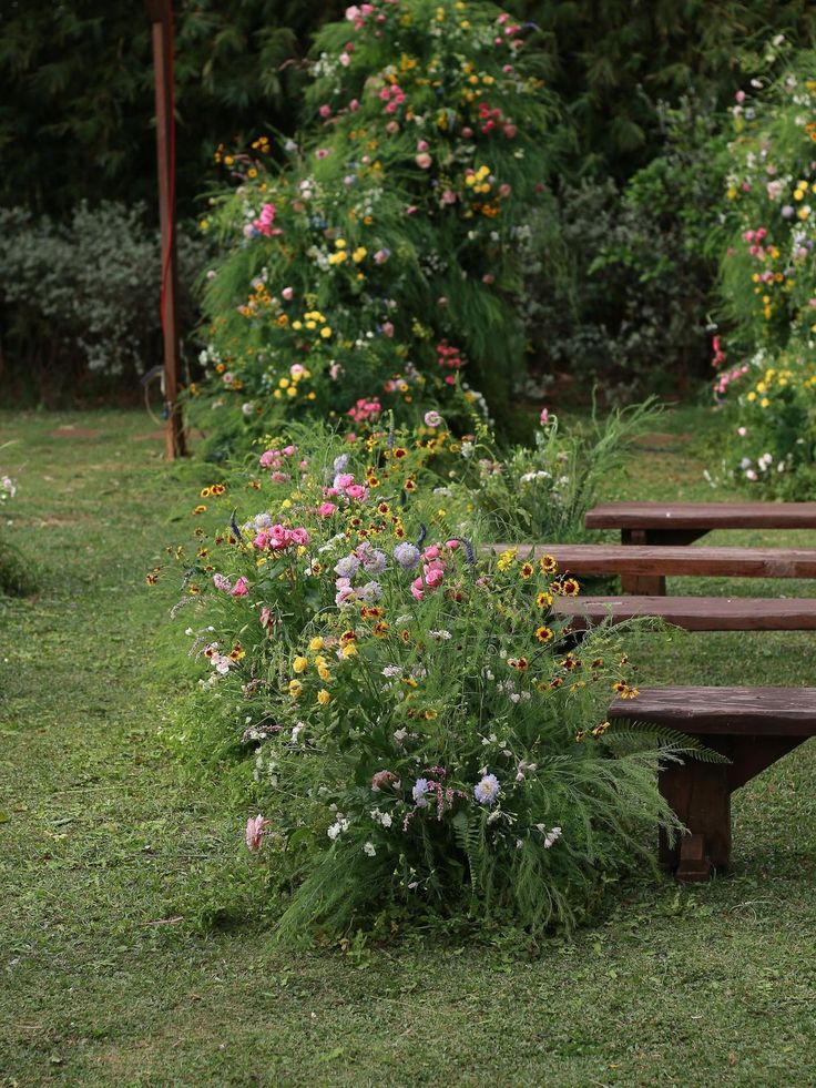 a wooden bench sitting in the middle of a lush green park filled with lots of flowers