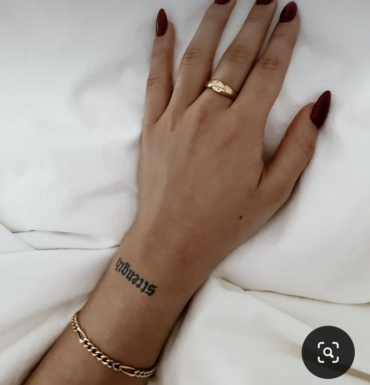 a woman's hand with a tattoo on her left wrist and gold chain bracelet