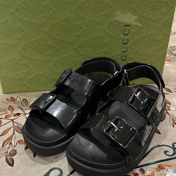 Gucci Isla Rubber Sandals Size 35 Brand New With Box And Dust Bag Designer Patent Leather Sandals With Buckle Closure, Gucci Luxury Sandals With Buckle Closure, Luxury Gucci Sandals With Buckle Closure, Modern Gucci Sandals With Round Toe, Designer Patent Leather Flat Sandals, Gucci Black Luxury Sandals, Black Gucci Luxury Sandals, Modern Gucci Sandals For Summer, Black Gucci Slides