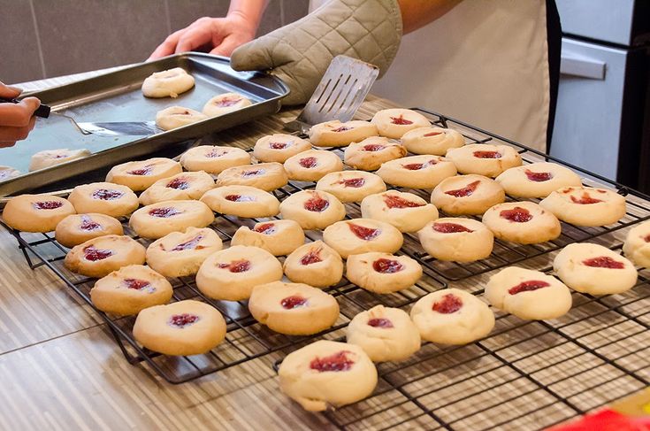 some cookies are cooling on a rack and someone is holding a spatula over them