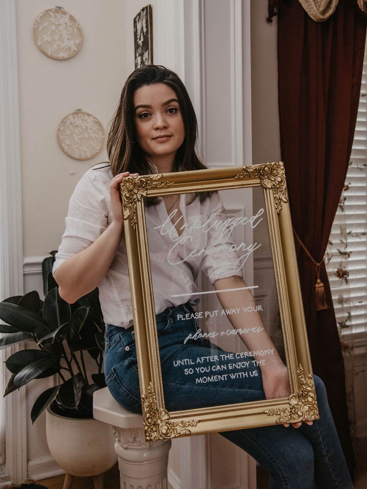 a woman sitting on a stool holding up a framed photo