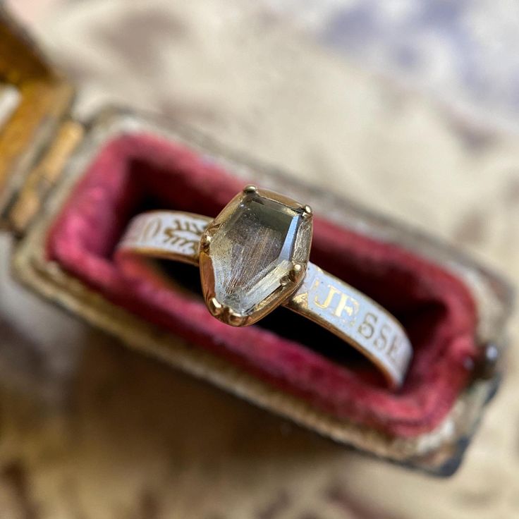 An untouched & pristine Georgian era mourning ring, rare in the unmarred white enamel that covers the rounded, convex shank; as well as the flawless coffin shaped crystal bezel that studs the front. Under the coffin, a stretch of tightly straight brown hair--still laying flat, prim and very orderly to this day.  The white color of the shank indicates the status of the deceased as unmarried or very young and alludes to pureness and innocence. The enamel, intact, solid and very finely done serves as the background for capital golden letters spelling out the deceased's details. There are several different flourishes in between the words of dedication on the shank, which is unusual and unique as more often than not in these examples there are typically maybe one or repeated motifs.  The uprigh Victorian Enamel Ring Engraved For Anniversary, Victorian Engraved Enamel Ring For Anniversary, Antique Enamel Ring With Rose Cut Diamonds, Antique Enamel Ring With Rose Cut Diamonds For Anniversary, Victorian Jewelry With Rose Cut Diamonds For Ceremonial Occasions, Victorian Engraved Rings For Memorial, Victorian Engraved Memorial Rings, Antique Engraved Enamel Ring For Anniversary, Heirloom Ring Jewelry For Memorial