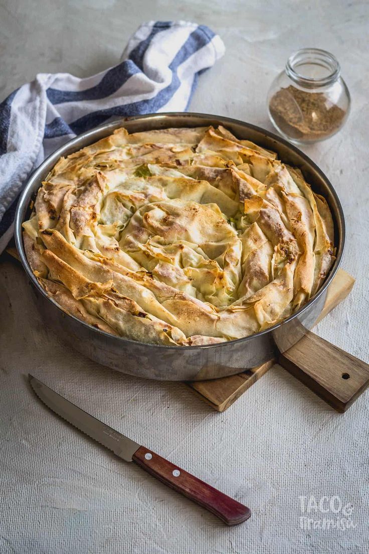 a pie sitting on top of a table next to a knife and bowl filled with food