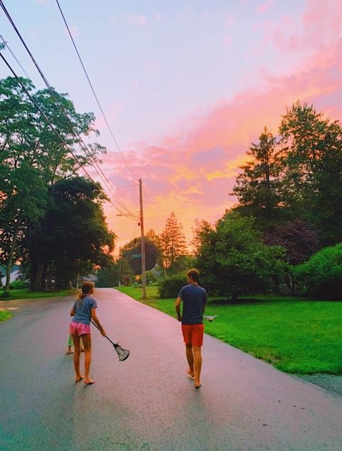 two people are walking down the street with tennis rackets in their hands as the sun sets