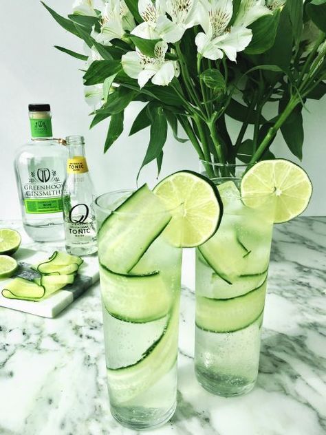 two glasses filled with cucumber and lemon slices on a marble table next to flowers