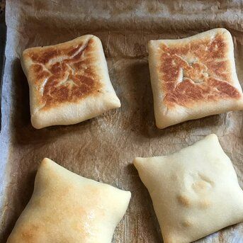 four square pieces of bread sitting on top of a sheet of wax paper next to each other