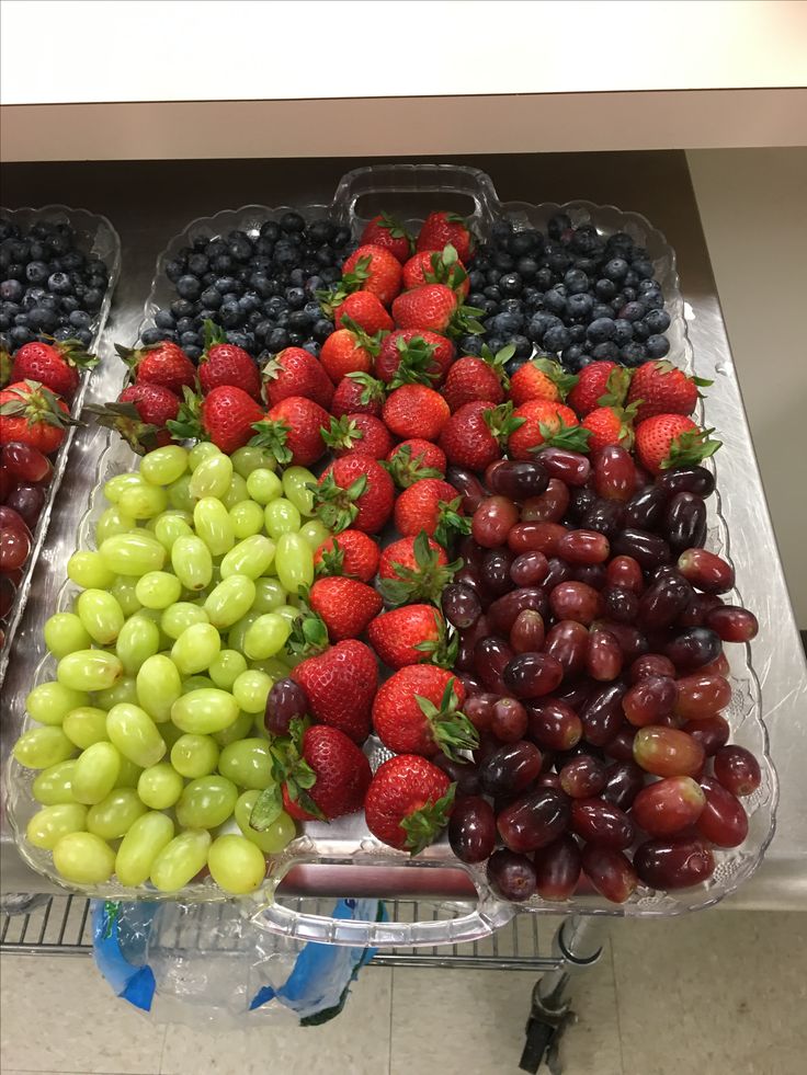 fruits are arranged in trays on the counter top at a grocery store, including grapes, strawberries, and plums