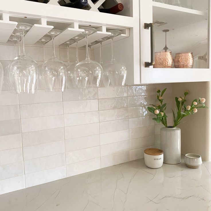 a kitchen counter with wine glasses and vases on the top shelf, next to a white tiled wall