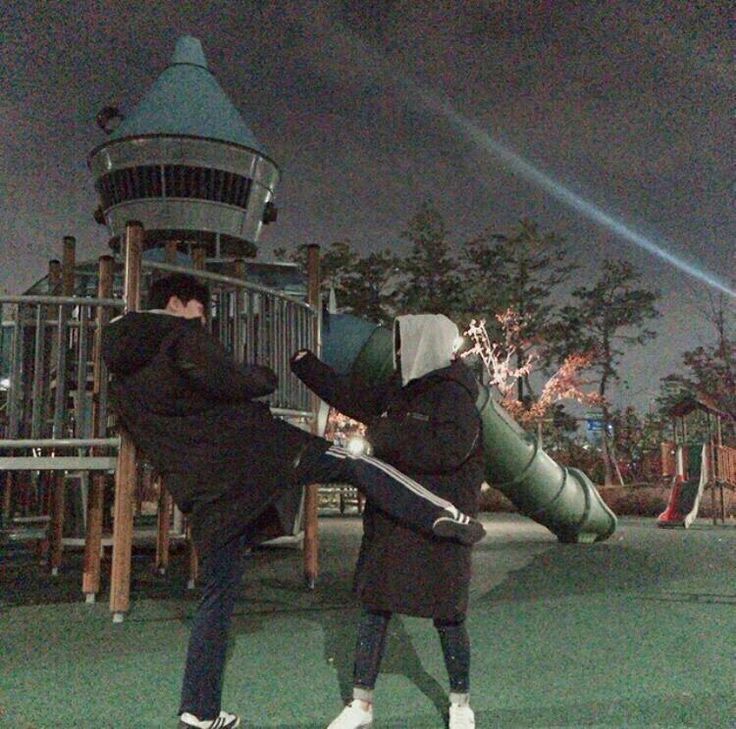 two people standing in front of a playground at night with one person holding an umbrella