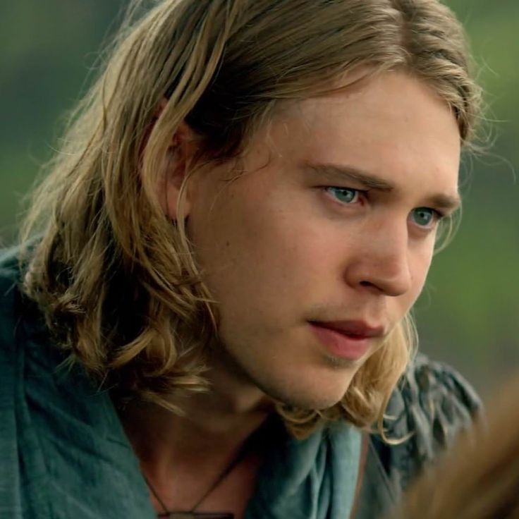 a close up of a person with long hair and blue eyes wearing a green shirt