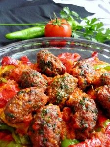 a glass bowl filled with meatballs and vegetables on top of a table next to a green pepper