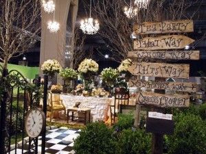 a table with flowers and signs on it in a room filled with greenery, chandeliers and decorations