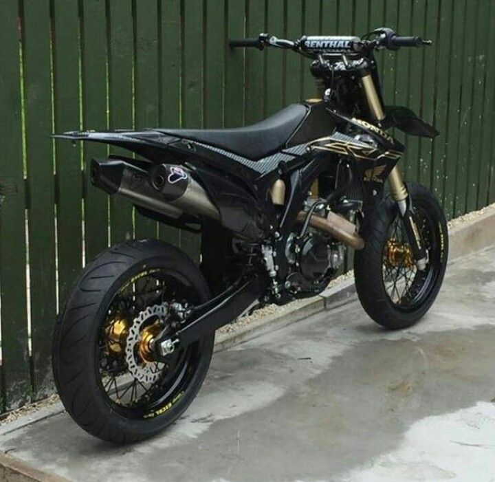 a black and gold motorcycle parked next to a green fence in front of a building