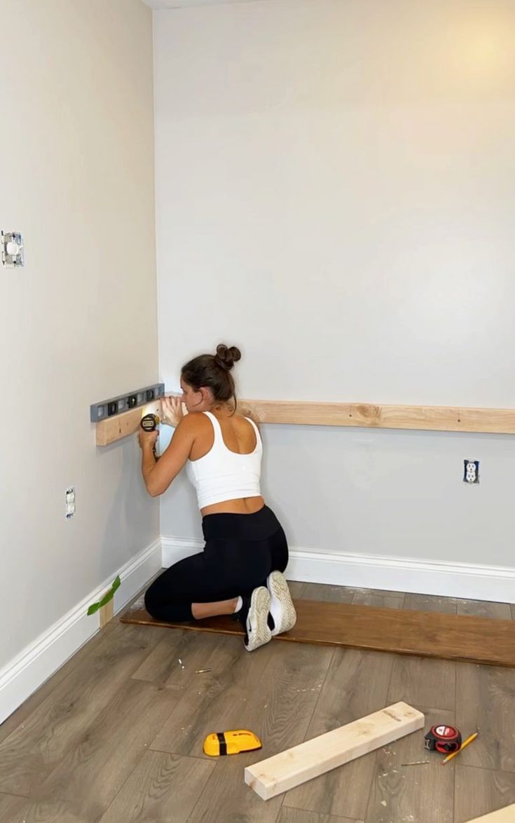 a woman kneeling on the floor with tools in front of her and working on wood planks