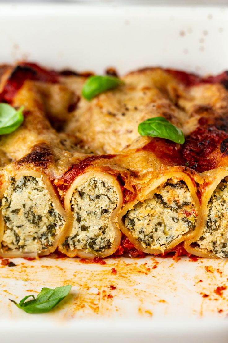 a white plate topped with lasagna rolls covered in cheese and spinach leaves