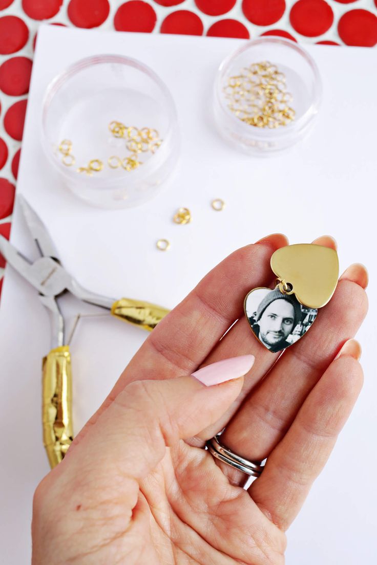 a hand holding a gold heart shaped brooch with a photo on it next to scissors and confetti