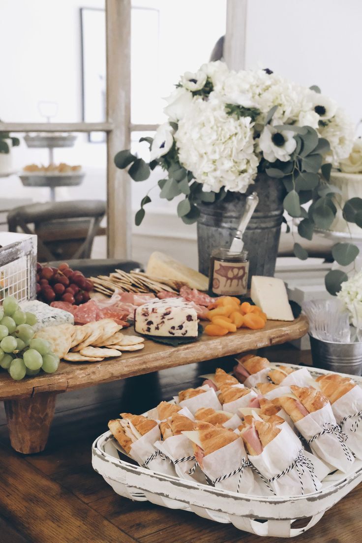 an assortment of cheeses, crackers and grapes on a table with flowers in the background