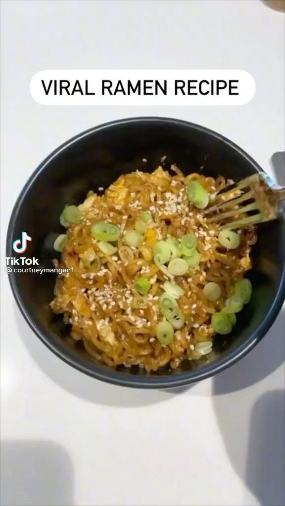 a black bowl filled with food on top of a white table next to a person's hand