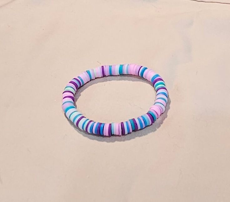 a colorful bracelet sitting on top of a sandy beach next to the ocean with a blue and pink bead around it