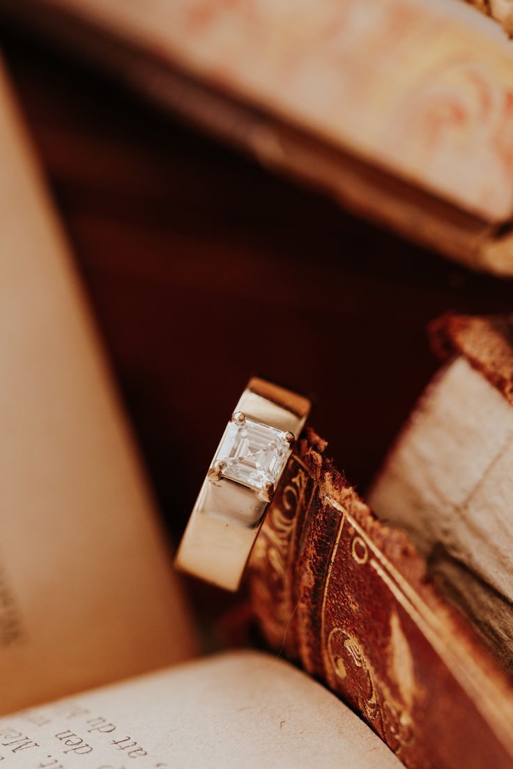 an open book with a ring on top of it next to some other books and papers