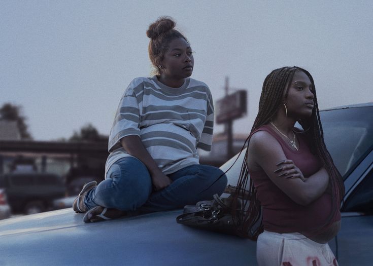 two women sitting on the hood of a car