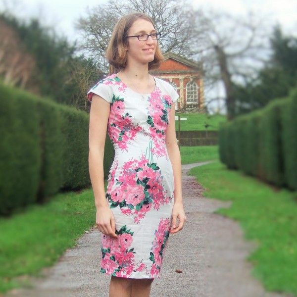 a woman standing on a path in front of some hedges and grass with her hands in her pockets