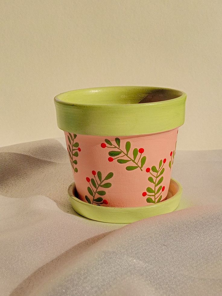 a pink and green planter with red berries on it sitting on a white surface