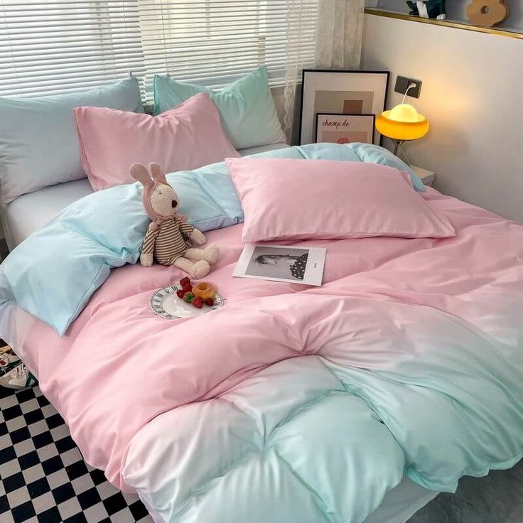 a bed with pink and blue sheets, pillows and a stuffed animal sitting on it