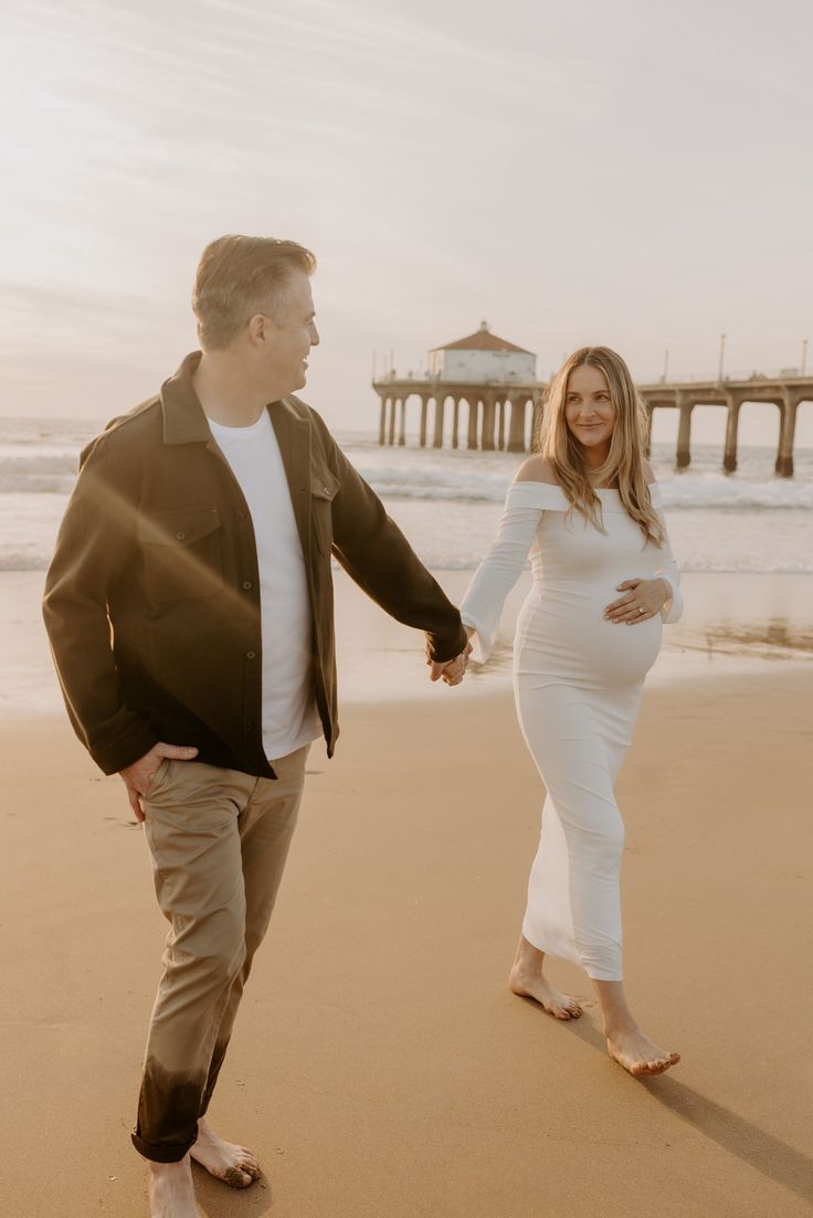 a pregnant woman walking on the beach with her husband