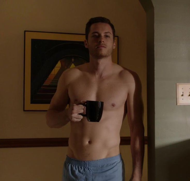 a shirtless man holding a coffee cup in his hand and looking at the camera