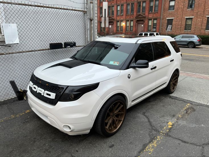 the white suv is parked on the side of the road near a fence and building