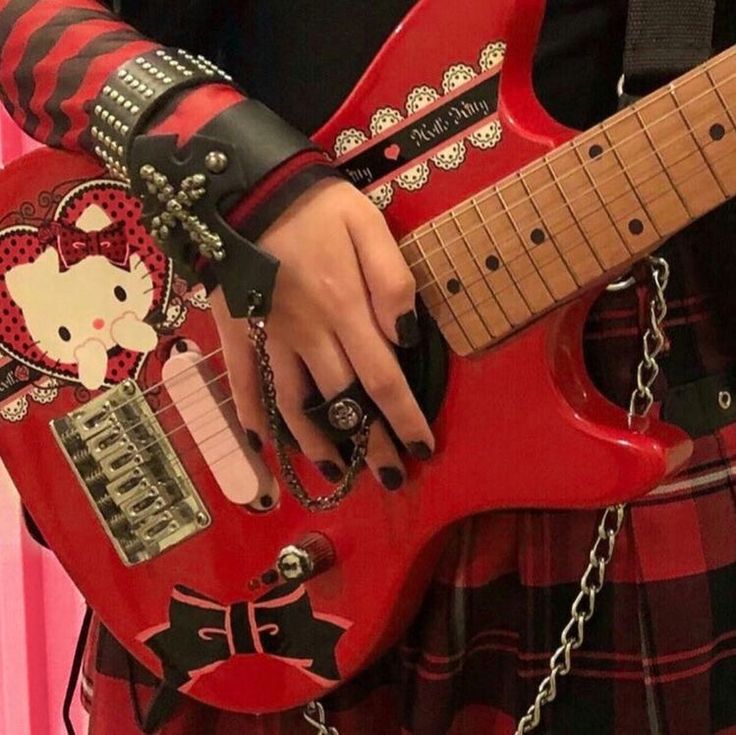 a person in a kilt holding a pink guitar with hello kitty stickers on it