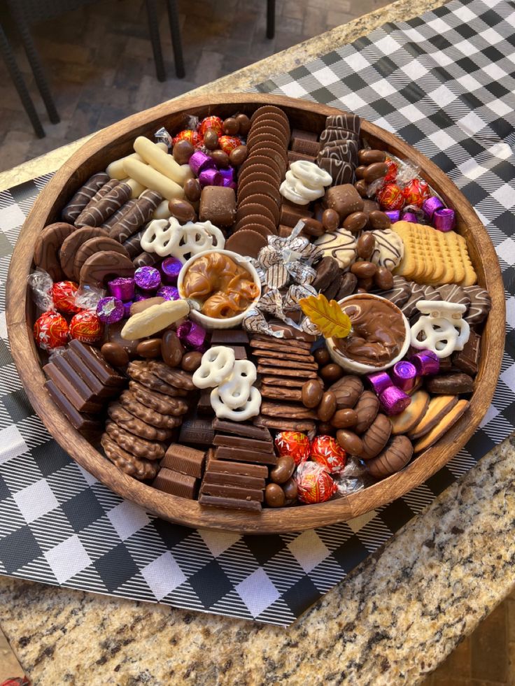 a wooden platter filled with lots of chocolate and candies on top of a checkered table cloth