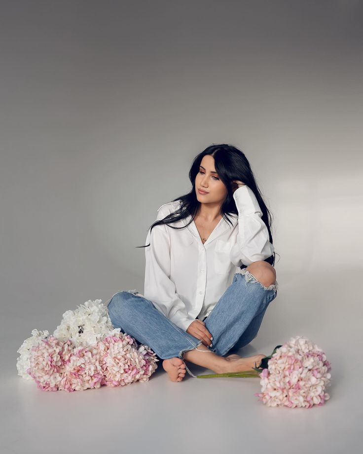 a woman sitting on the ground with flowers in front of her and posing for a photo