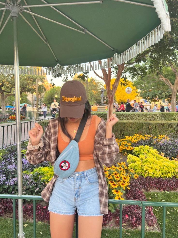 a woman holding an umbrella in front of her face and wearing a hat on top of her head