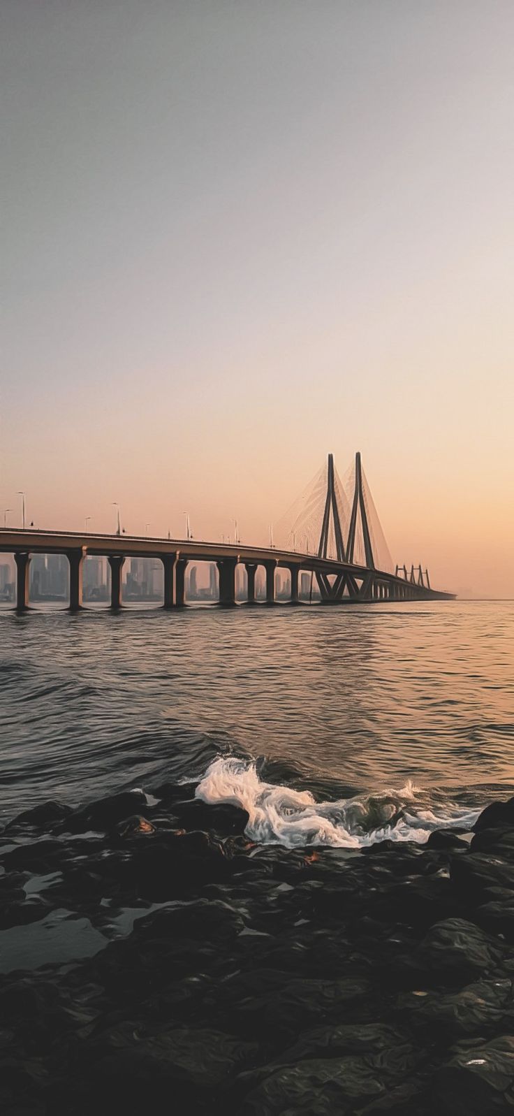 the sun is setting behind a bridge over water with waves crashing in front of it