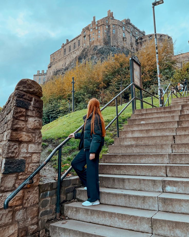 a woman with red hair is standing at the top of stairs in front of a castle