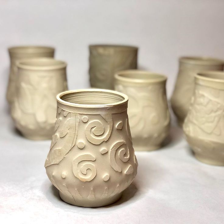 several white vases are lined up on a tableclothed surface, with one in the center surrounded by smaller ones