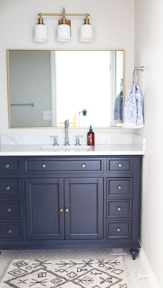 a bathroom vanity with blue cabinets and white counter tops, along with a rug on the floor