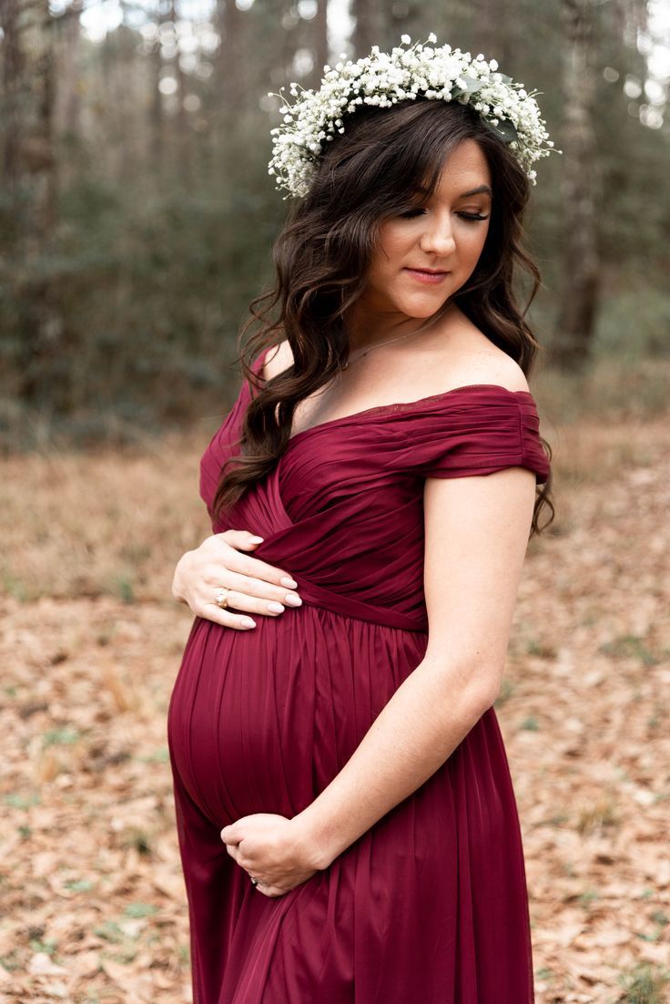 a pregnant woman wearing a flower crown poses for a photo in the woods with her hands on her belly