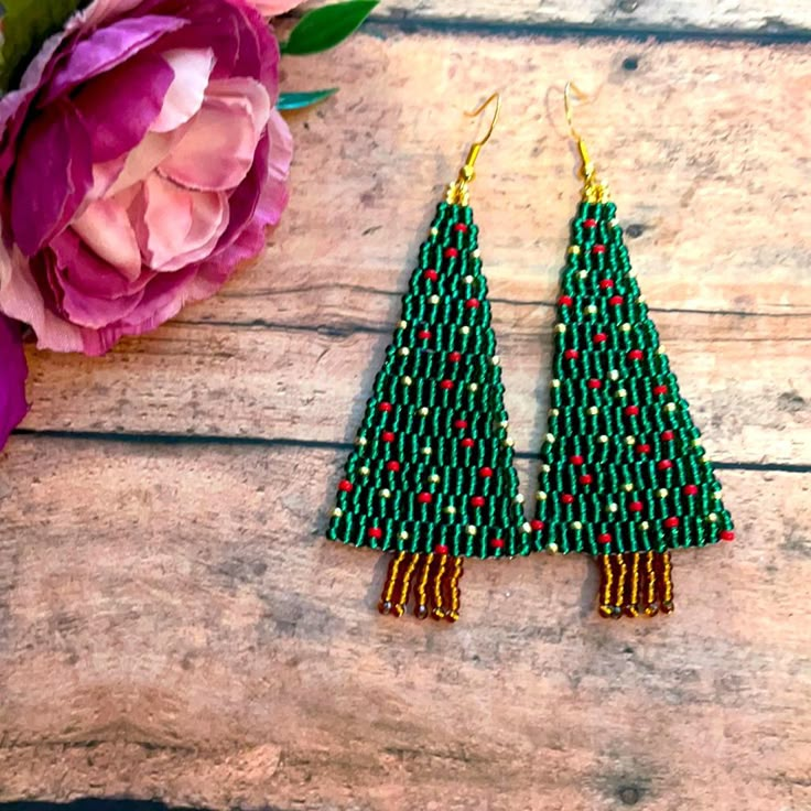 the beaded christmas tree earrings are on display next to a pink flower and purple peonie