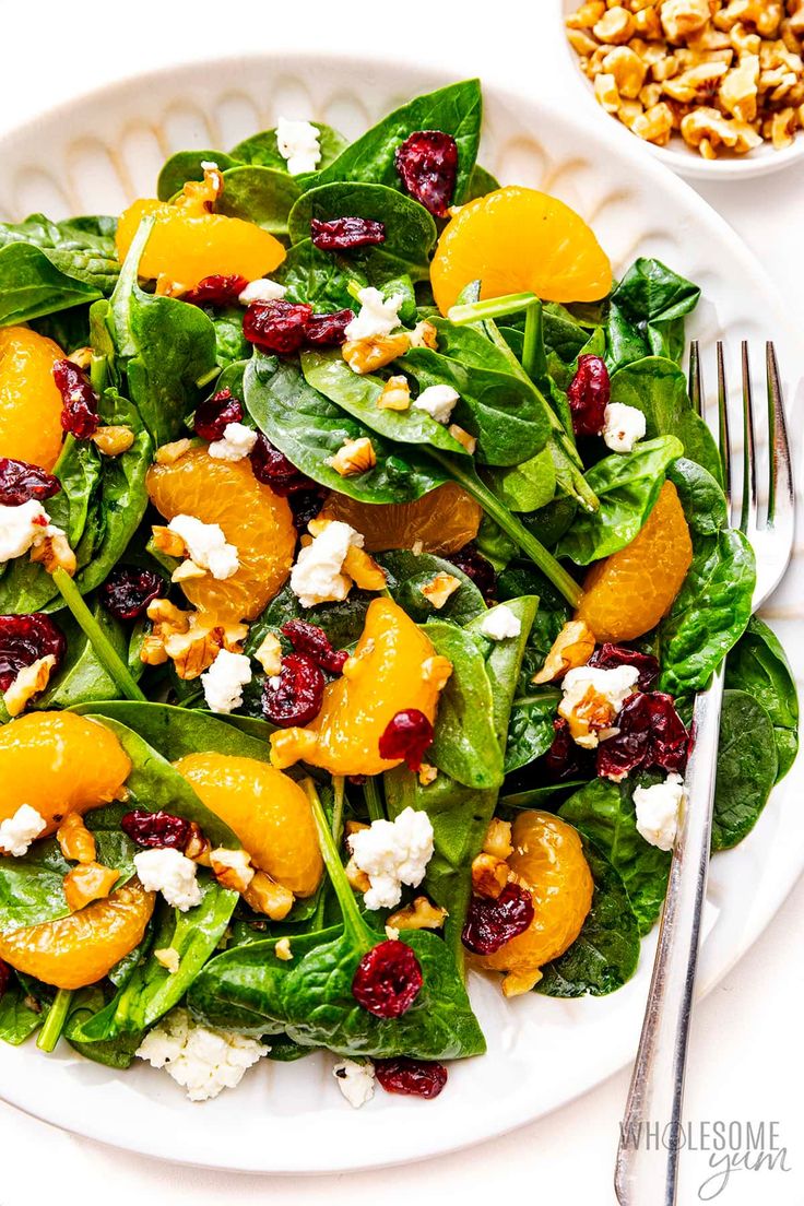 spinach salad with oranges, cranberries and feta cheese on a white plate