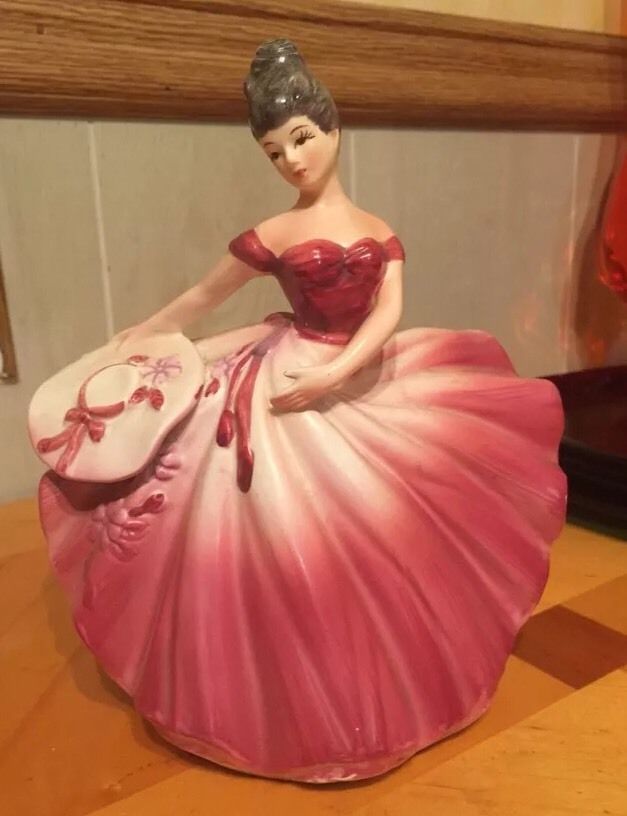 a ceramic figurine of a woman in a pink dress sitting on a table