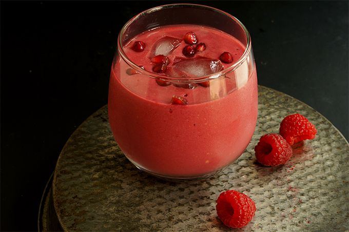 raspberry smoothie in a glass with ice cubes on a plate next to raspberries